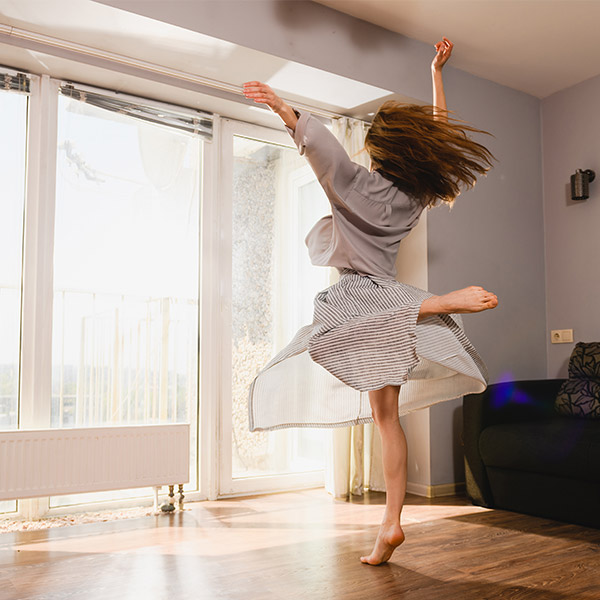 Woman dancing on wooden floor in bright living room.