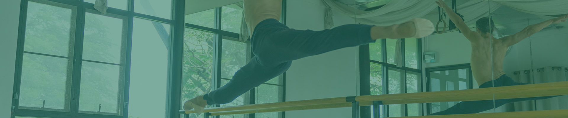 Dancer practicing on a ballet barre with reflection in studio mirror, highlighting sprung floors for optimal performance.