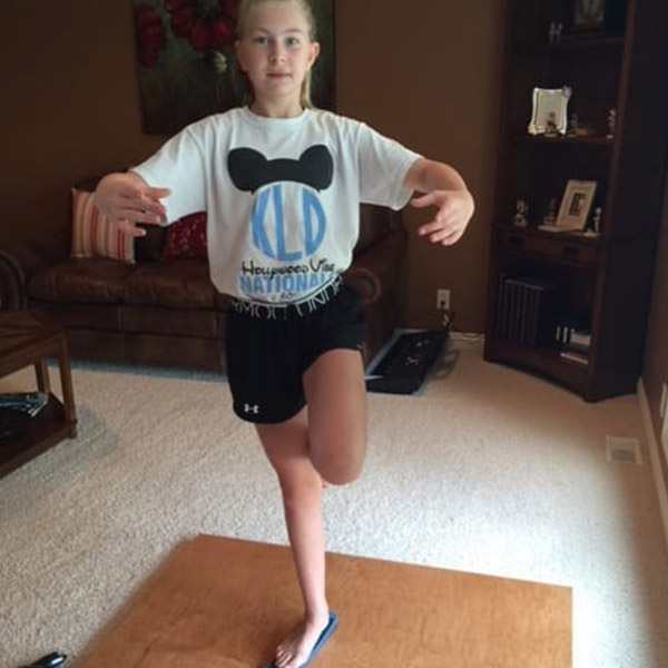 Young dancer balancing on one foot on a wooden sprung dance floor in a home setting, demonstrating the floor's use in dance practice.