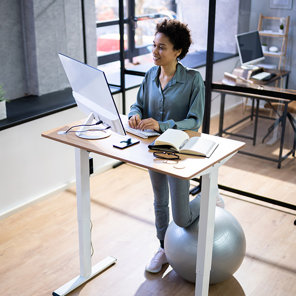 Person using standing desk with stability ball in modern office setting.