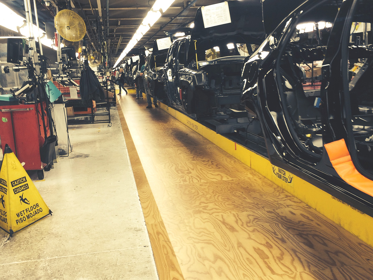 Industrial automotive assembly line with sprung floors for worker comfort and safety, featuring unfinished vehicles on production line.