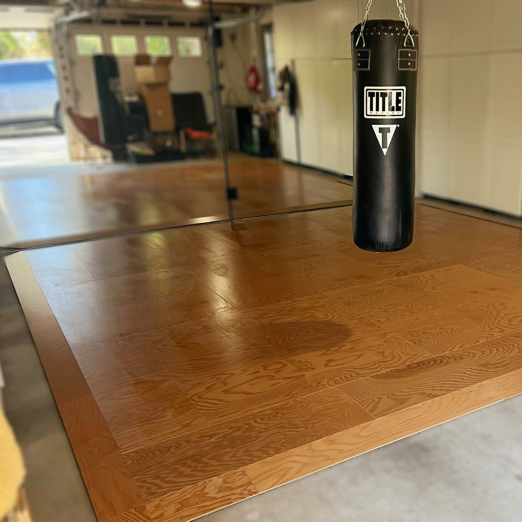 Precision-engineered wooden sprung exercise floor in a home garage with a hanging heavy bag, ideal for dance, yoga, and workout routines.