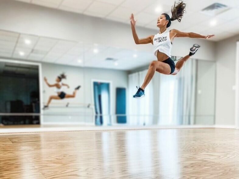 Dancer leaping gracefully on a Sprung Floors precision practice dance floor in a bright studio with mirrored walls.